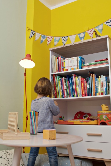 Kinderzimmer Makeover mit Wayfair: Kind sitzt an weißem Buecherregal mit Holzgriffen und Holzfüßen