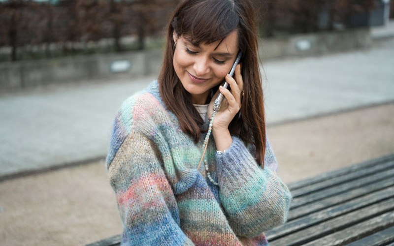 Die besten Handyketten / Smartphoneketten: Frau mit buntem Pullover trägt farblich passende Handykette von StudioNooks